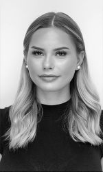 Porträt einer Person mit langen, blonden Haaren vor neutralem Hintergrund.